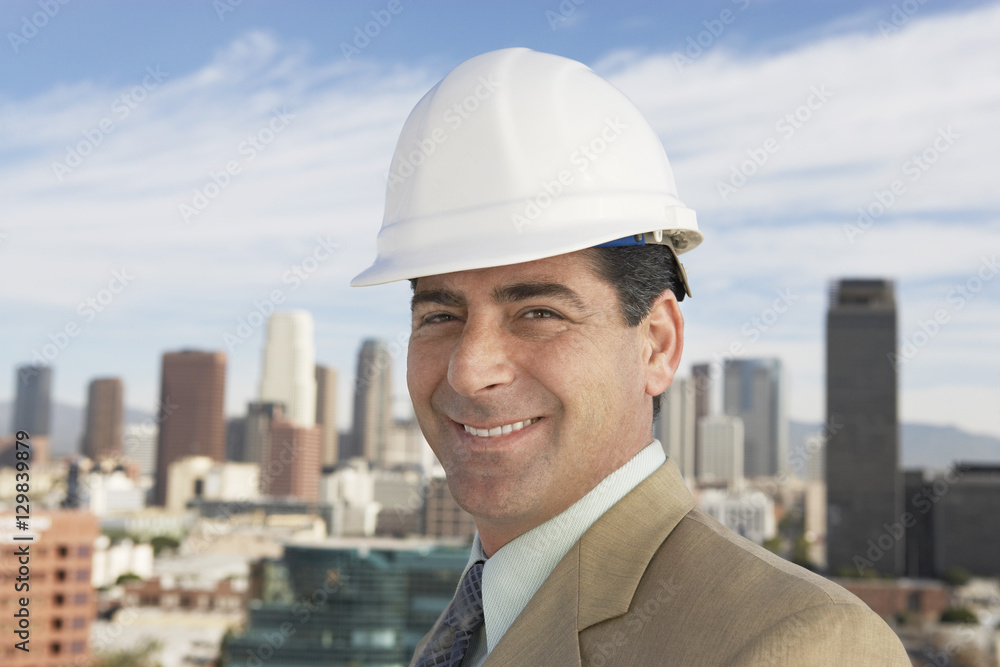 Closeup portrait of a smiling confident man wearing hard hat against urban buildings Closeup portrait of a smiling confident man wearing hard hat against urban buildings