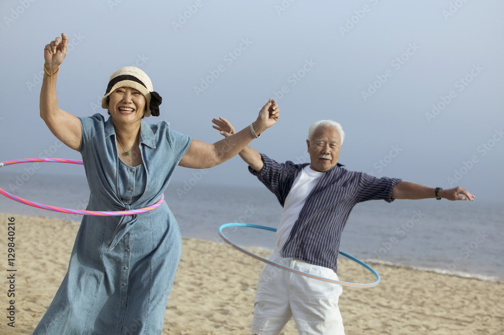 Couple with hula hoops on beach - obrazy, fototapety, plakaty 