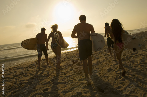 Photography Group of friends with surfboards running towards ocean at sunset