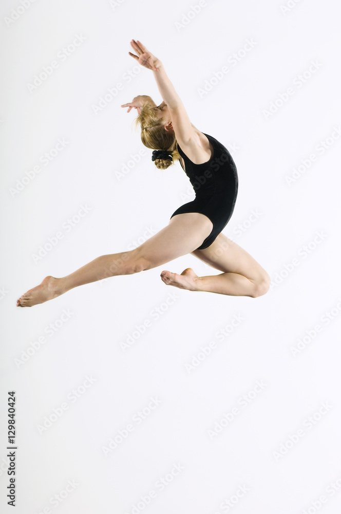 Side view of a female gymnast leaping in air against white background
