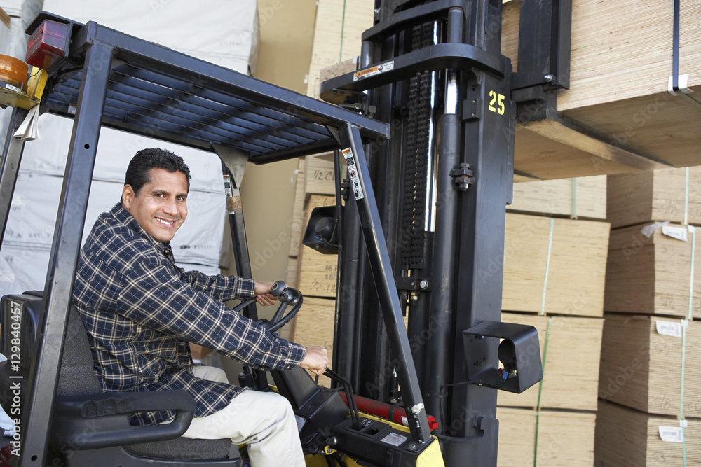 Portrait of happy mature warehouse worker stacking wood by forklift Portrait of happy mature warehouse worker stacking wood by forklift