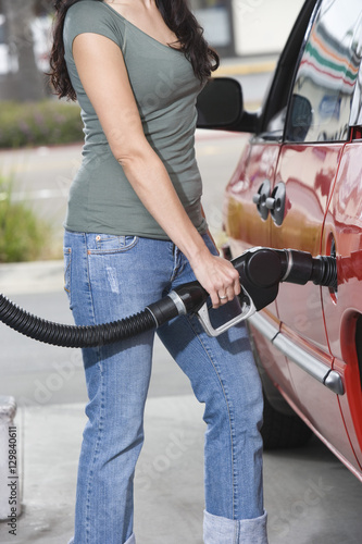 Mid section of a woman refueling her red car at a service station