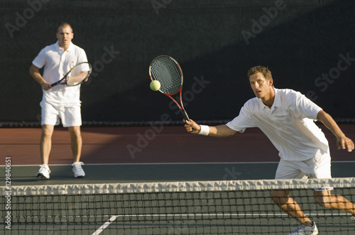 Mixed doubles player hitting tennis ball with partner in the background © moodboard