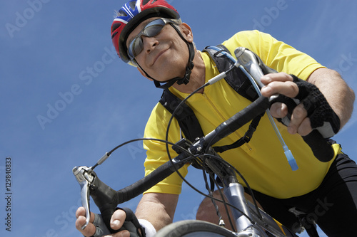 Low angle view of happy senior male cyclist riding bicycle against sky