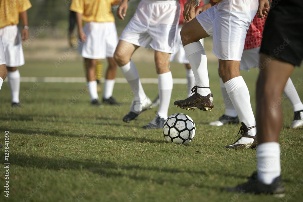 Fototapeta premium Low section of players playing football with teammates in the background