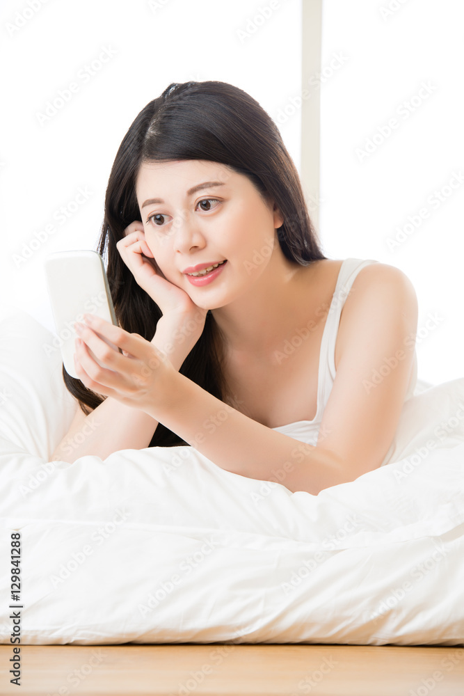 Young smile asian woman reading smart phone on bed