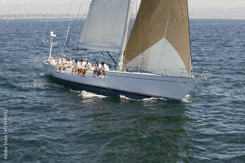 Group of crew members sitting on the side of a sailboat in the ocean