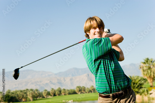 Portrait of a happy young man swinging club at golf course