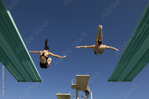 Obraz na płótnie Rear view of two women diving from diving boards against clear blue sky