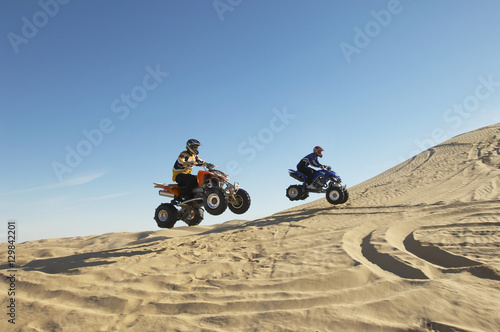 Side view of two men doing wheelies on quad bikes in the desert