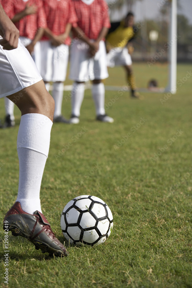 Low section of a football player taking freekick with oppositions in the background
