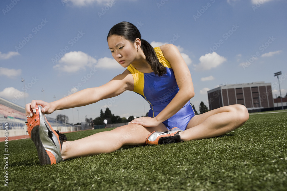 Young Asian female athlete stretching on the field