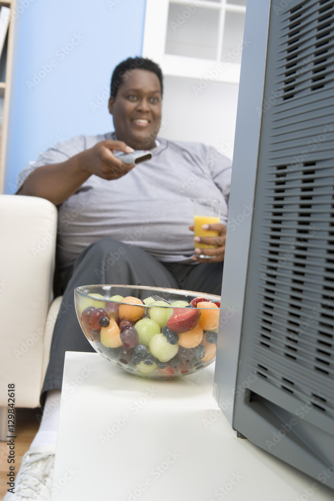 Happy African obese man watching television while holding glass of juice Happy African obese man watching television while holding glass of juice