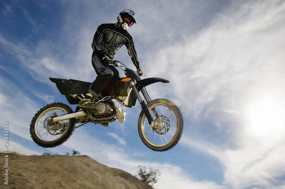 Low angle view of motocross racer in midair against cloudy sky Low angle view of motocross racer in midair against cloudy sky