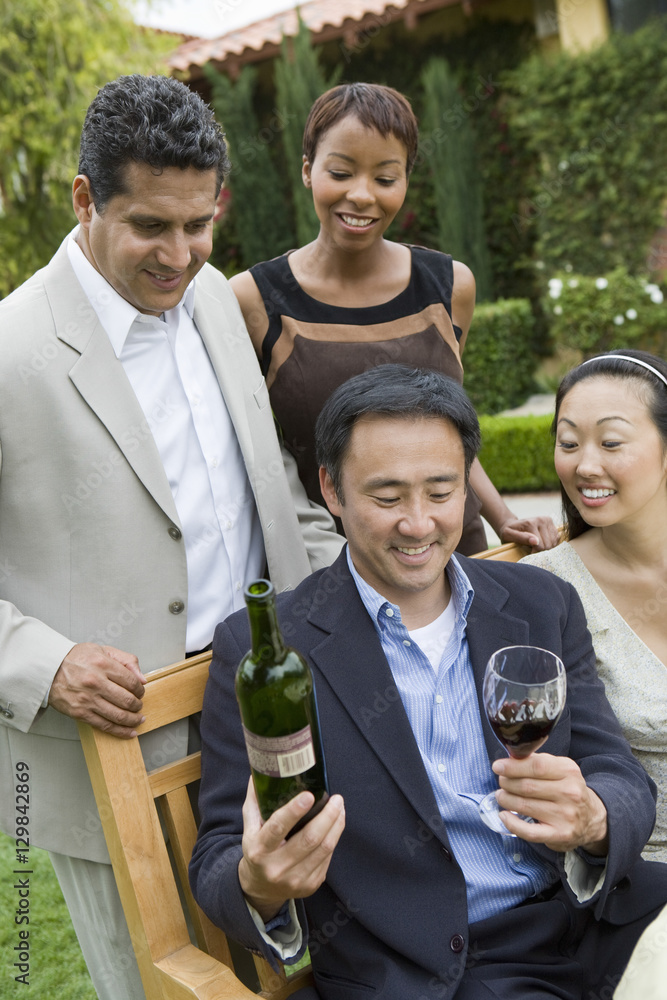 Middle aged man holding wine bottle and glass with friends in park Middle aged man holding wine bottle and glass with friends in park