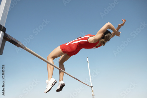 Tableau sur toile Low angle view of a female high jumper in midair over bar against blue sky