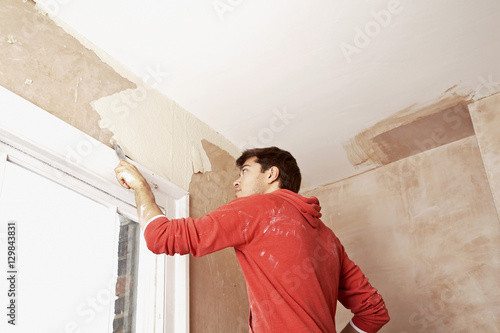 Fotografi Low angle view of man scraping paint off wall in unrenovated room