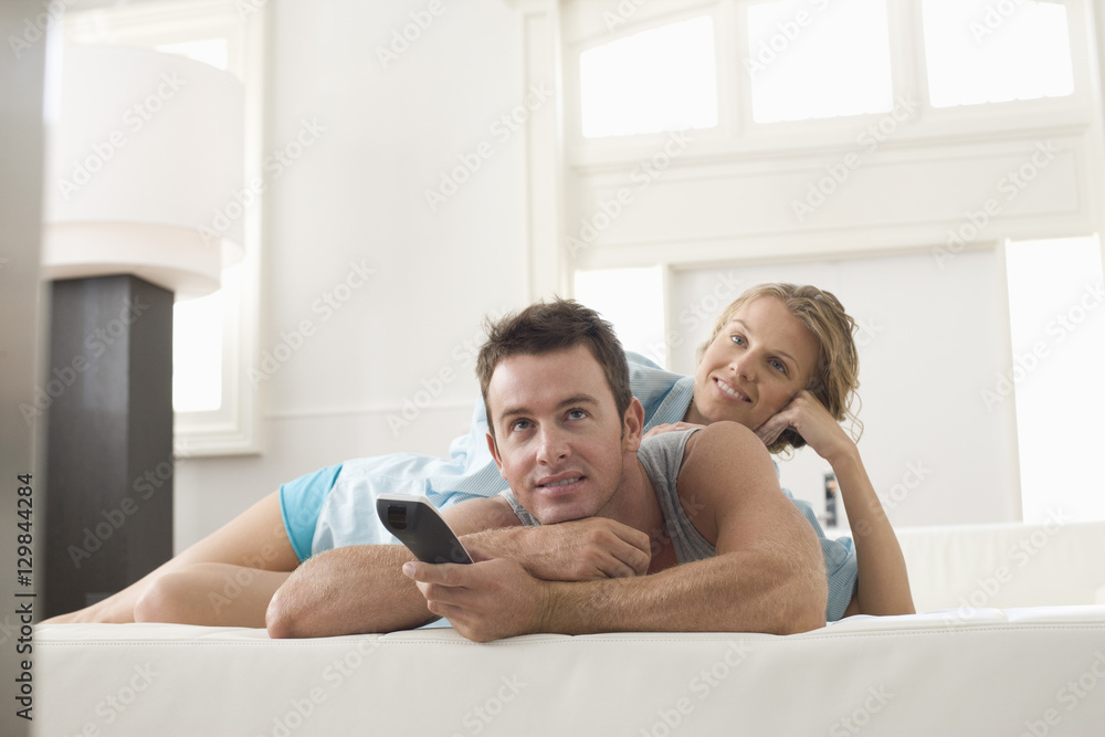 Happy young couple lying on bed and watching TV at home Happy young couple lying on bed and watching TV at home