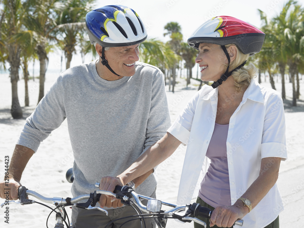 Obraz premium Happy senior couple wearing helmets with bicycles on tropical beach
