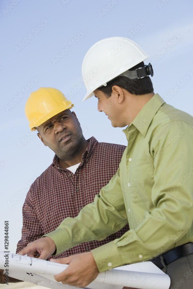 Architect and foreman in discussion with blueprint against sky Architect and foreman in discussion with blueprint against sky
