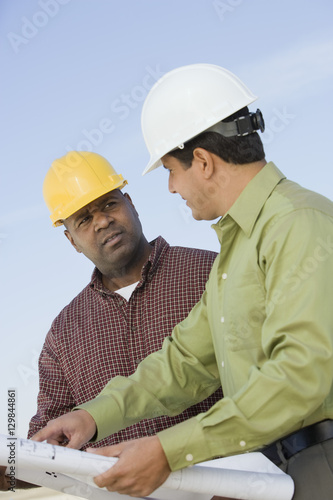 Architect and foreman in discussion with blueprint against sky
