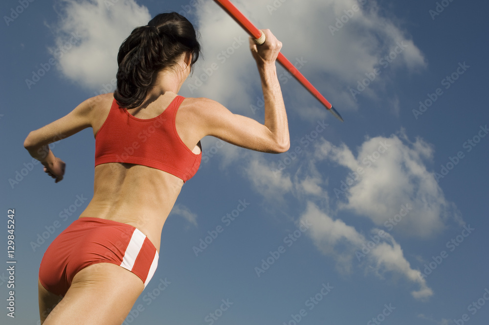 Rear view of female athlete in sportswear throwing javelin against cloudy sky