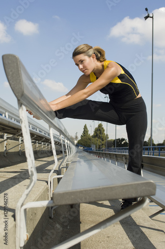 Fit Caucasian woman in sportswear working out at stadium bench