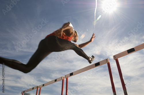 Low angle view of a male athlete jumping hurdle against the sky photo