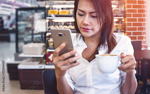 Asia women who drink coffee and look at his cell phone at the sa photo