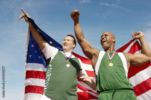 Male athletes with medal and American flag against sky