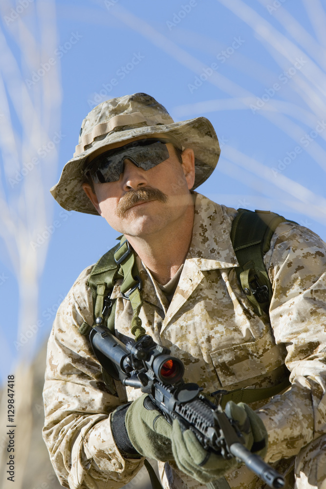 Middle aged soldier holding rifle against sky