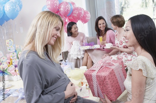Happy woman giving a gift to an expecting mother at baby shower