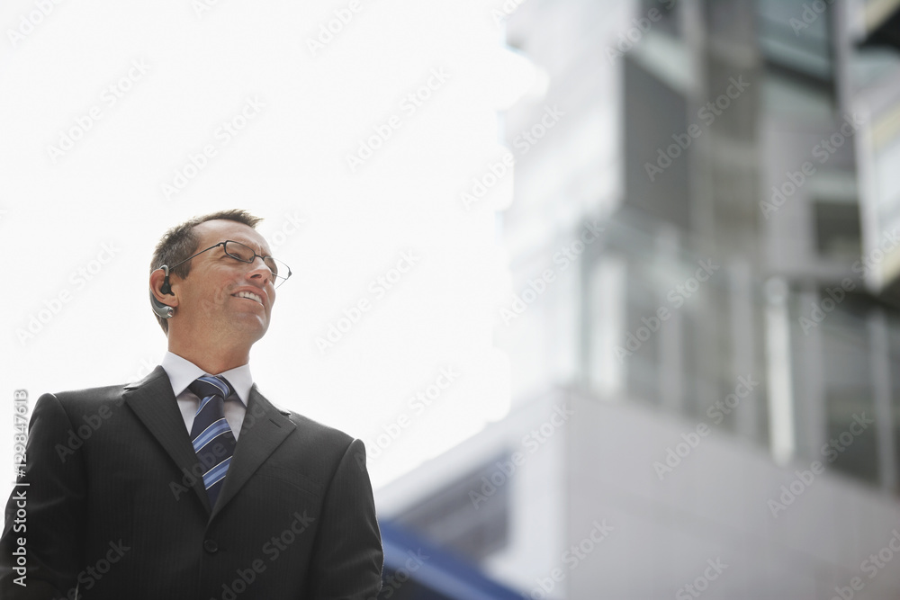 Low angle view of confident businessman wearing wireless headset against sky Low angle view of confident businessman wearing wireless headset against sky