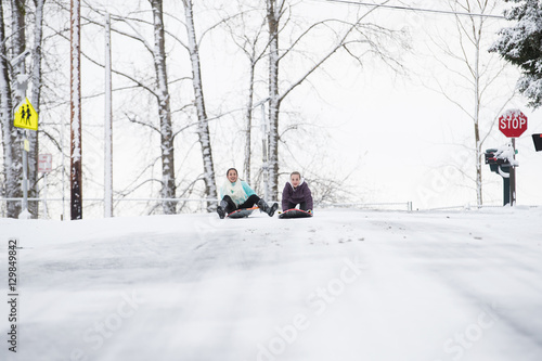 Two young girls sledding down hill in ice and snow