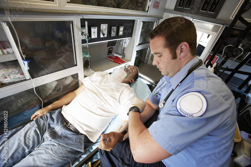 Male EMT professional taking pulse of a man inside ambulance
