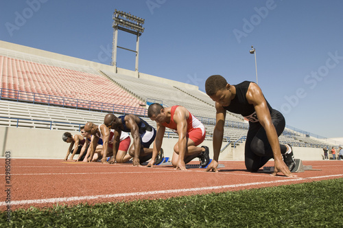 Group of multiethnic male runners at starting blocks in racetrack