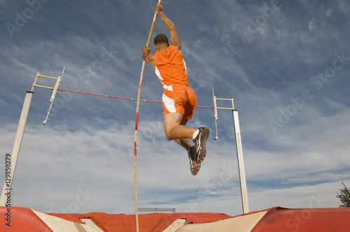 Tableau sur toile Male athlete pole vaulting against cloudy sky