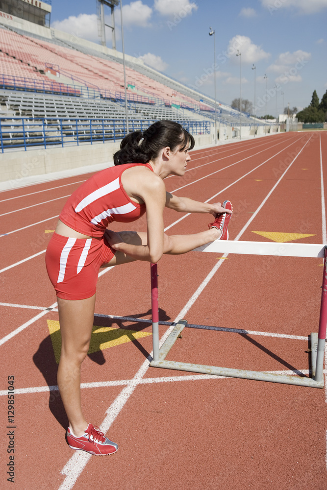Full length of female athlete stretching leg before hurdle race