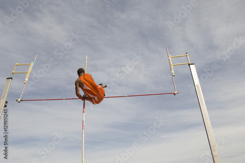 Photos Low angle view of male pole vaulter clearing bar against cloudy sky