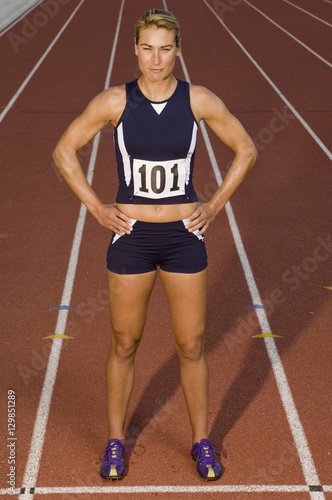 Portrait of confident female athlete with hands on hips in racetrack