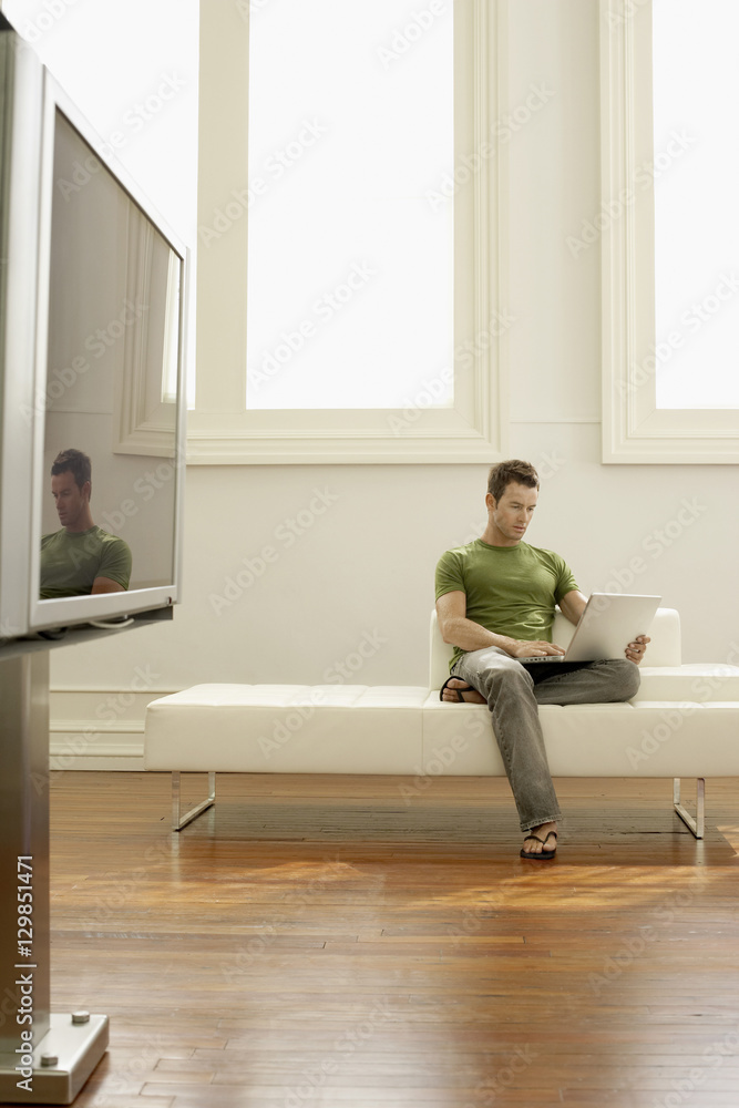 Full length of young man using laptop on sofa in modern apartment