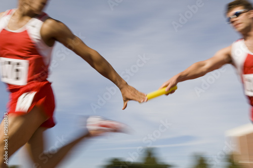Blurred motion male runners passing baton in relay race photo