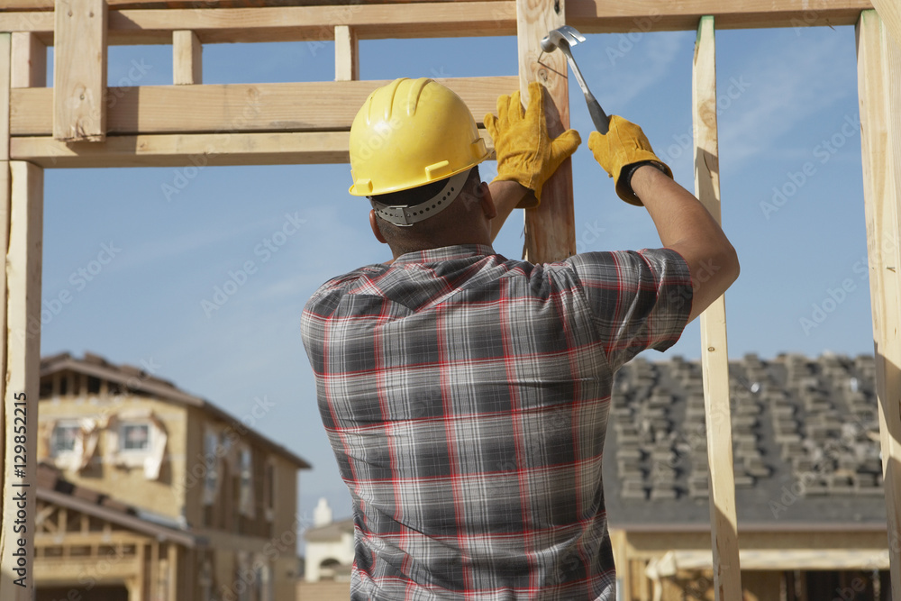 Rear view of a construction worker in hardhat working on timber frame Rear view of a construction worker in hardhat working on timber frame