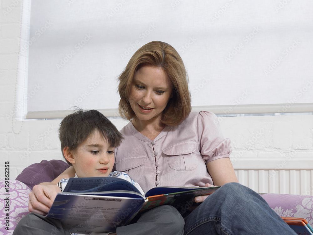 Loving mother and son reading book together on bed at home Loving mother and son reading book together on bed at home