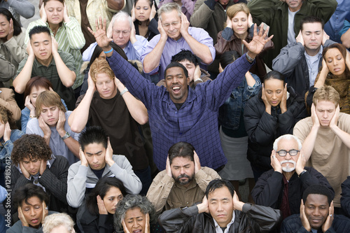 Portrait of a happy African American man raising hands while people covering their ears