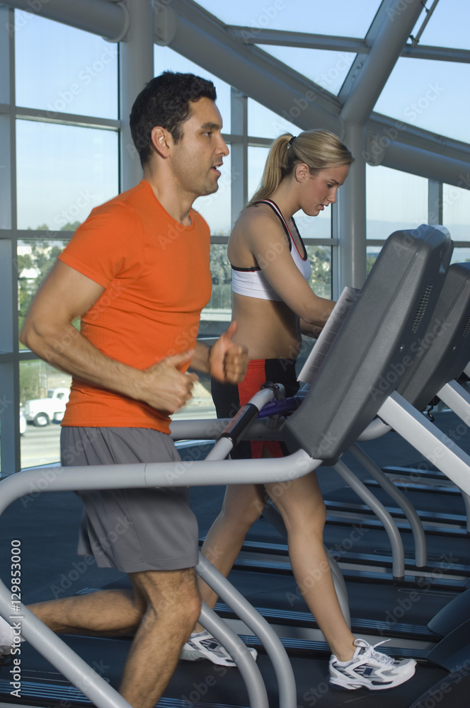 Side view of man and woman on treadmill at gym Side view of man and woman on treadmill at gym
