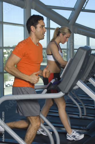 Side view of man and woman on treadmill at gym © moodboard