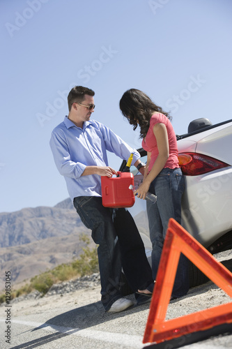Full length of a couple with oil can standing by car
