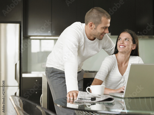 Happy Young couple looking at each other while using laptop in modern kitchen © moodboard