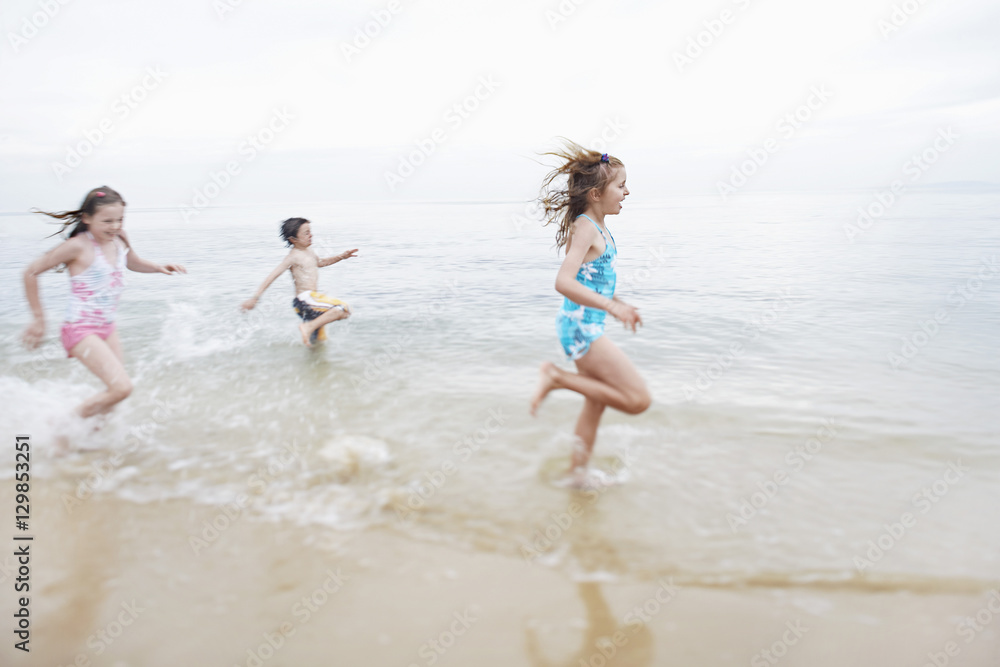 Excited young children running in surf at beach